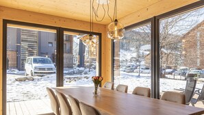 A modern dining area with a wooden table and chairs, large windows offering a view of a snowy parking lot and buildings.