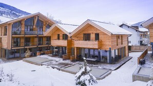 A modern wooden lodge with multiple balconies and large windows, situated in a snowy mountainous area.