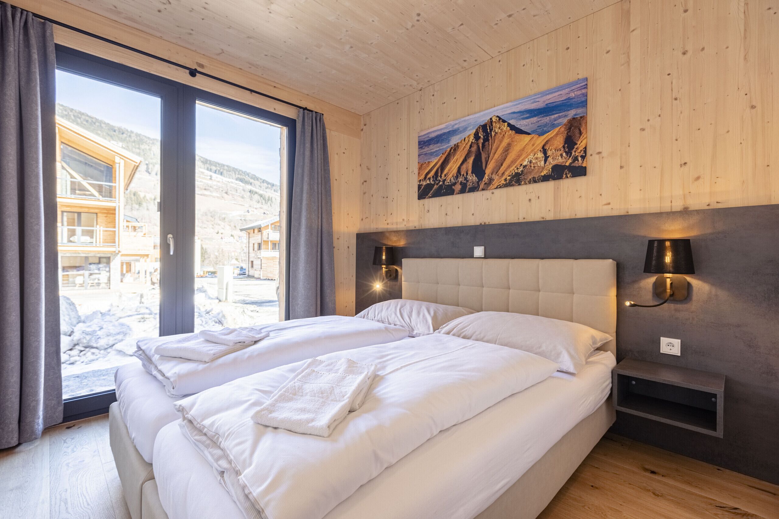 Een slaapkamer met twee bedden, een groot raam, houten wanden en uitzicht op bergen.