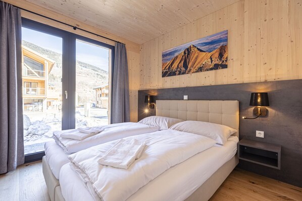 Un dormitorio con dos camas, un ventanal grande, paredes de madera y vistas a la montaña.