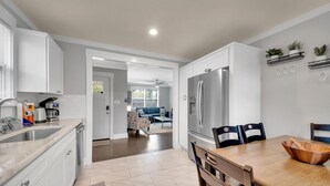 Una cocina moderna con armarios blancos, un refrigerador de acero inoxidable y un comedor con una mesa y sillas de madera.