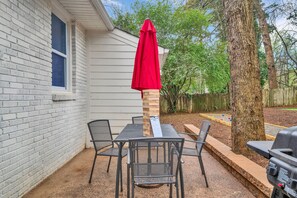 A patio with a table and chairs, a red umbrella, and a grill.