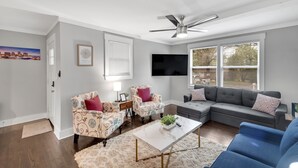 Una sala de estar moderna con un sofá seccional, sillones estampados, un televisor de pantalla plana y un ventilador de techo.