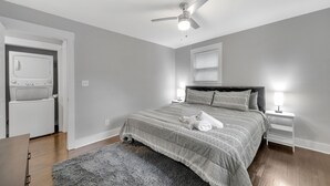 Un dormitorio con cama, ventilador de techo, mesita de noche con lámpara, puerta y horno empotrado.