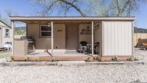 A small wooden structure labeled "Kaitlin's Cottage" with a kitchenette, seating area, and a door. - Kaitlins Kottage at Serenity Hills Zion (Glendale)