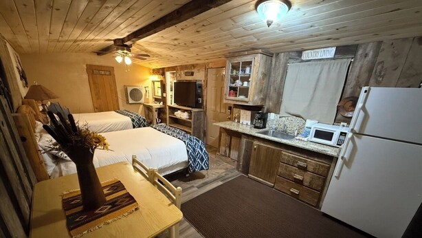 A cozy cabin interior with two beds, a dining table, a kitchen area, and a sign reading 'COUNTRY LIVING'. - Kaitlins Kottage at Serenity Hills Zion (Glendale)