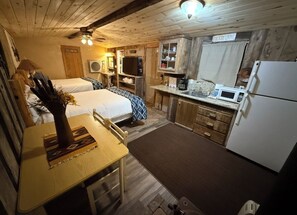 A cozy cabin interior with two beds, a dining table, a kitchen area, and a sign reading 'COUNTRY LIVING'.