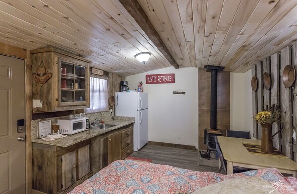 A rustic retreat with a wooden ceiling, a kitchen with a microwave, and a sign reading "Rustic Retreats".