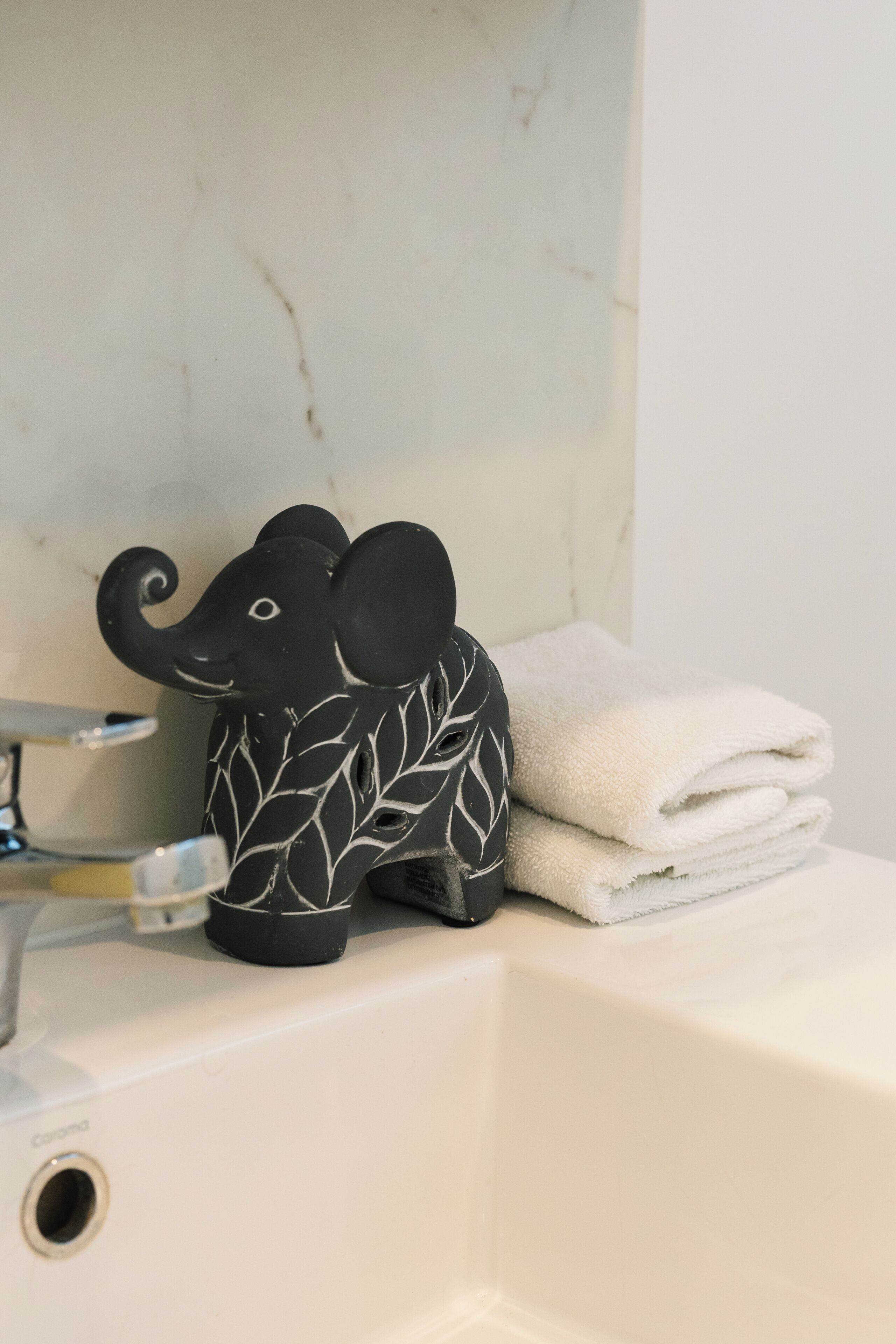 Un baño con lavamanos, una pila de toallas y una figurita decorativa de elefante.
