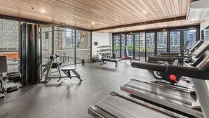 Une salle de sport équipée de machines de cardio, de poids et offrant une vue sur les bâtiments grâce à de grandes fenêtres.