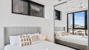 Une chambre d’hôtel avec un grand lit, un miroir, une fenêtre donnant sur la ville et un ventilateur de plafond.