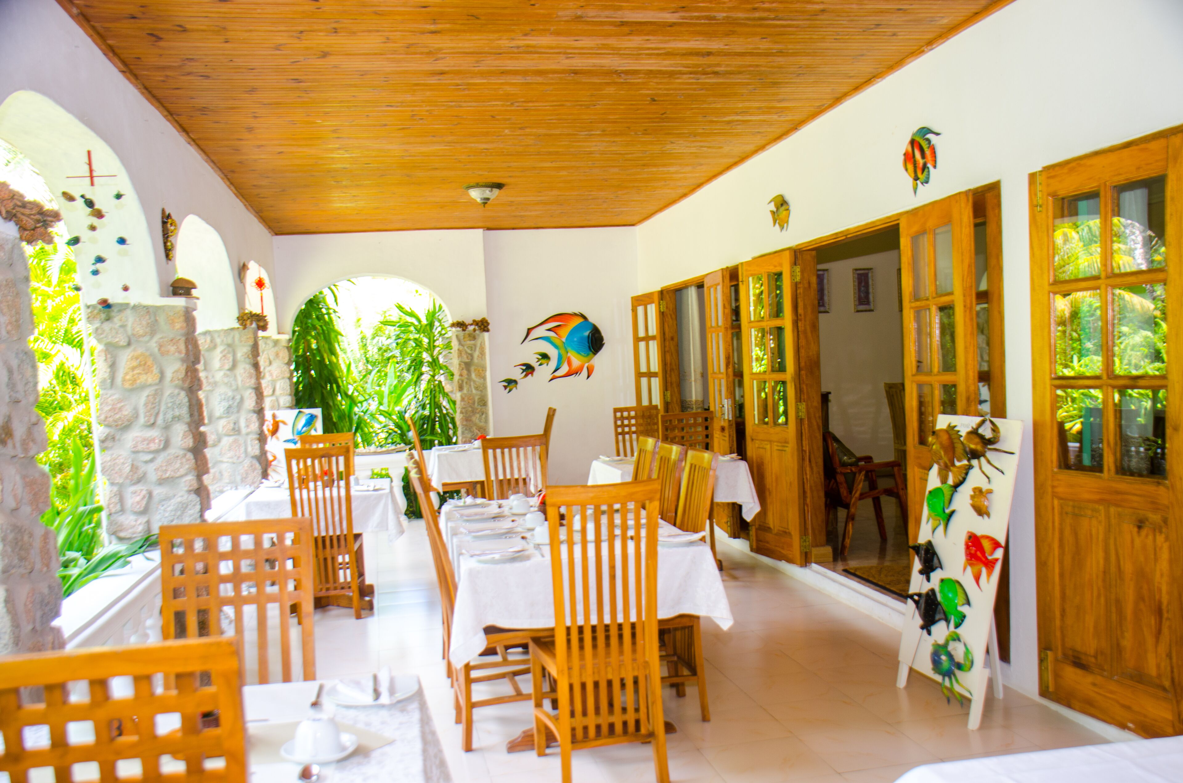 A restaurant with wooden tables and chairs, stone walls, and a view of greenery.