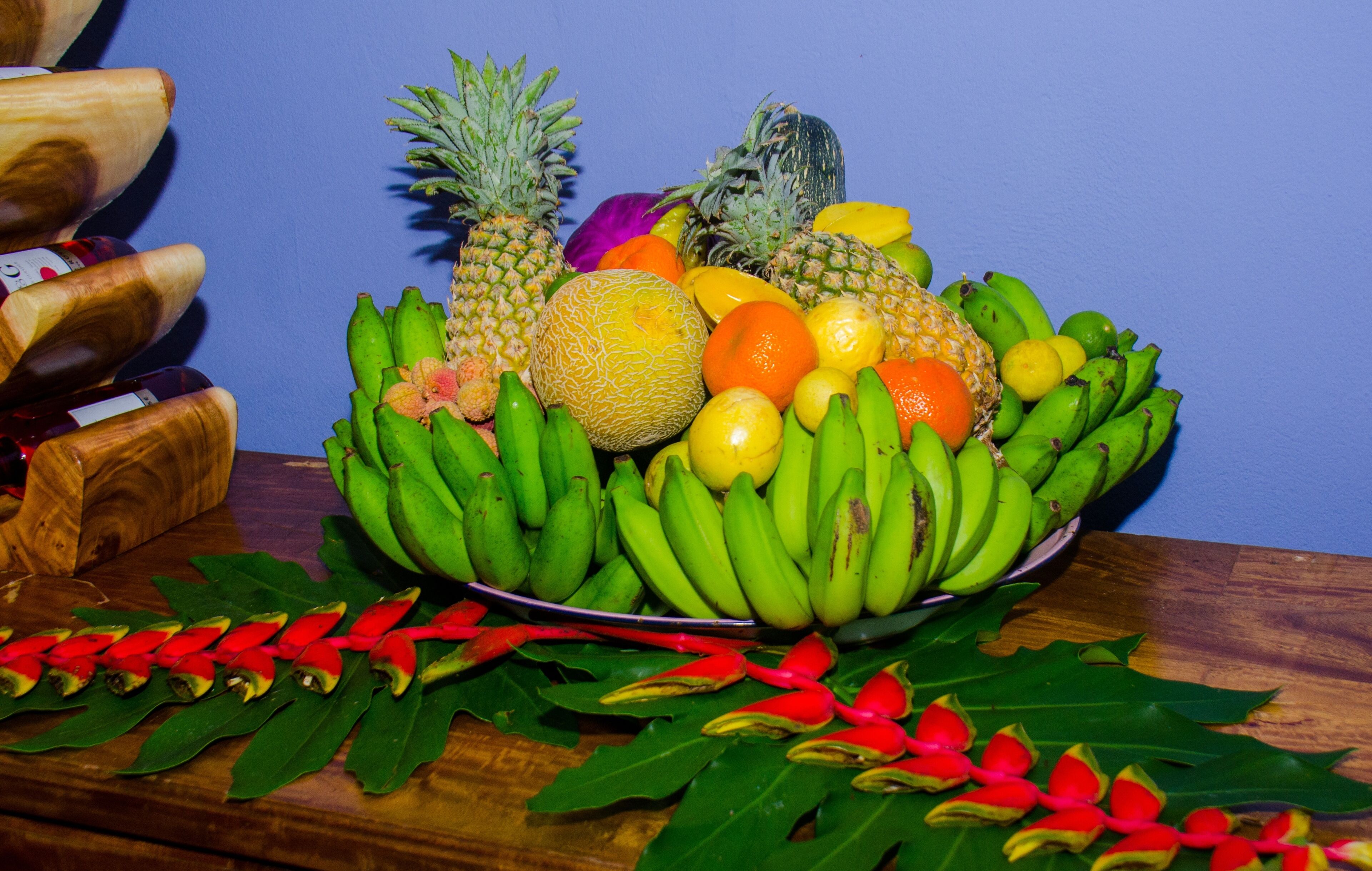 Una ciotola di frutta con banane, ananas, arance e altra frutta su un tavolo di legno.