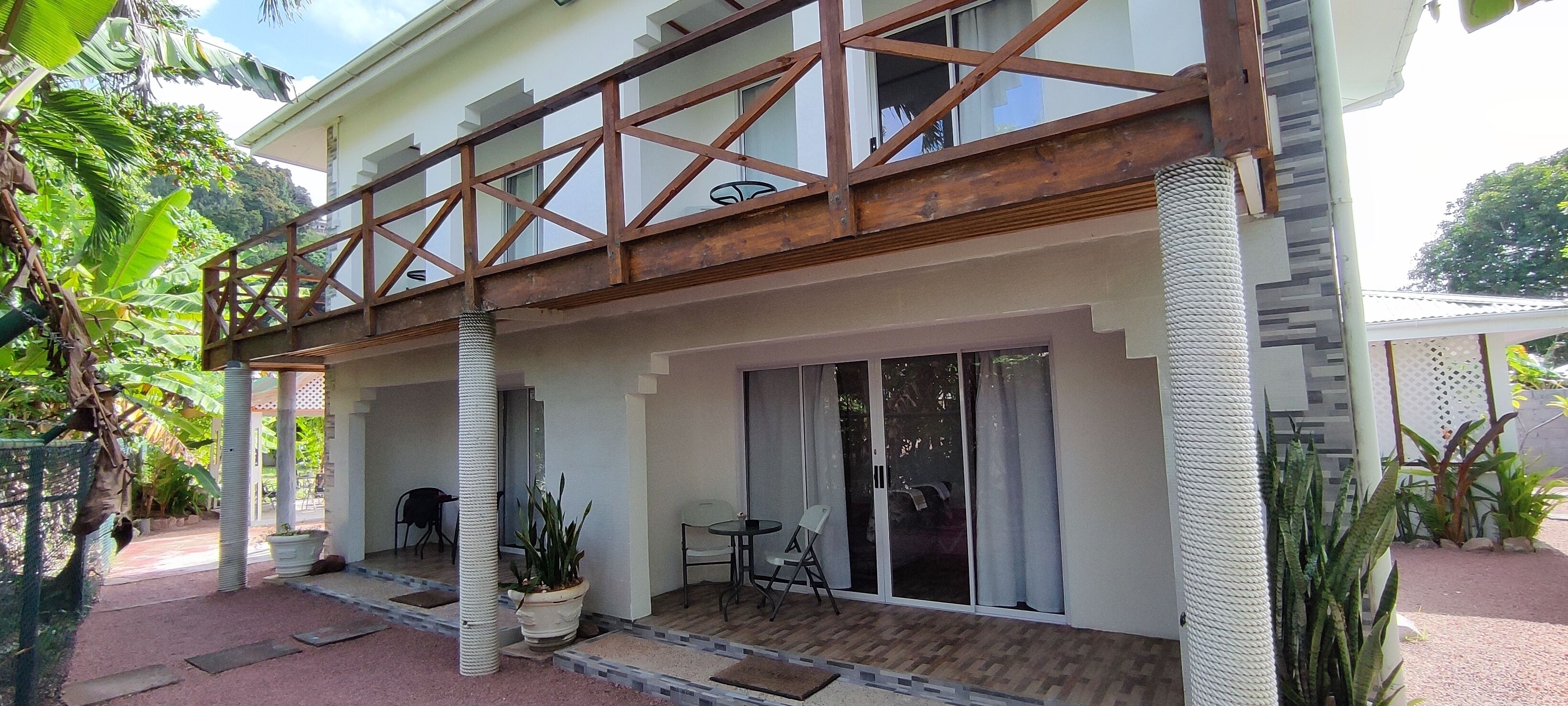 A two-story building with a balcony, large sliding glass doors, and potted plants.