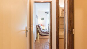 Ein schmaler Flur mit Fliesenboden führt zu einem Schlafzimmer mit Bett und Nachttisch.