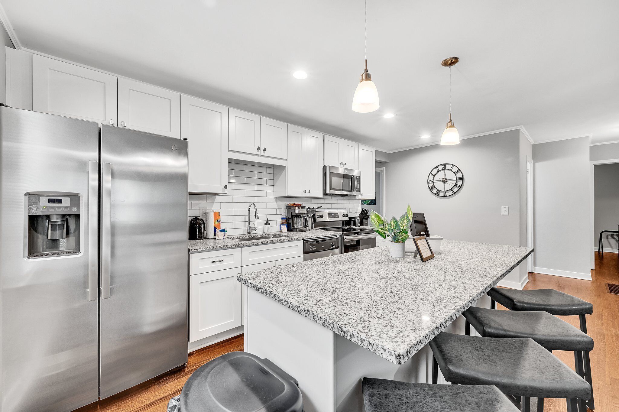 A modern kitchen with stainless steel appliances, white cabinets, a granite countertop, and a clock on the wall.