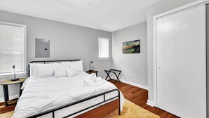 Un dormitorio con cama, mesitas de noche, un calentador en la pared, una ventana y una puerta.
