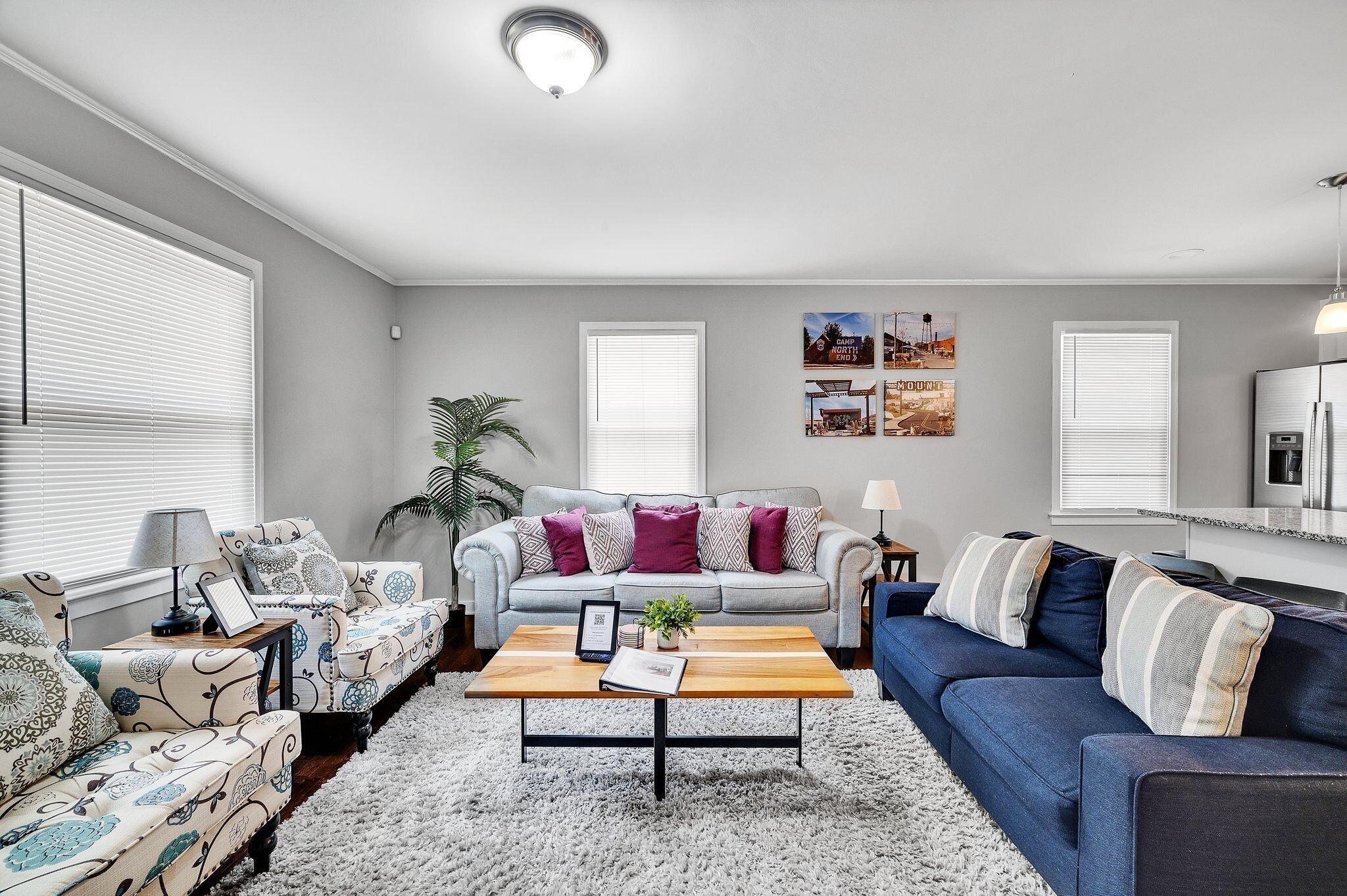 A modern living room with a grey sofa, blue sofa, and patterned armchairs. There is a coffee table with a book and a plant.