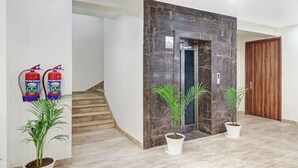 A modern interior with a marble staircase, a wooden door, and two fire extinguishers mounted on the wall. - Hotel the Archer (Gurugram)