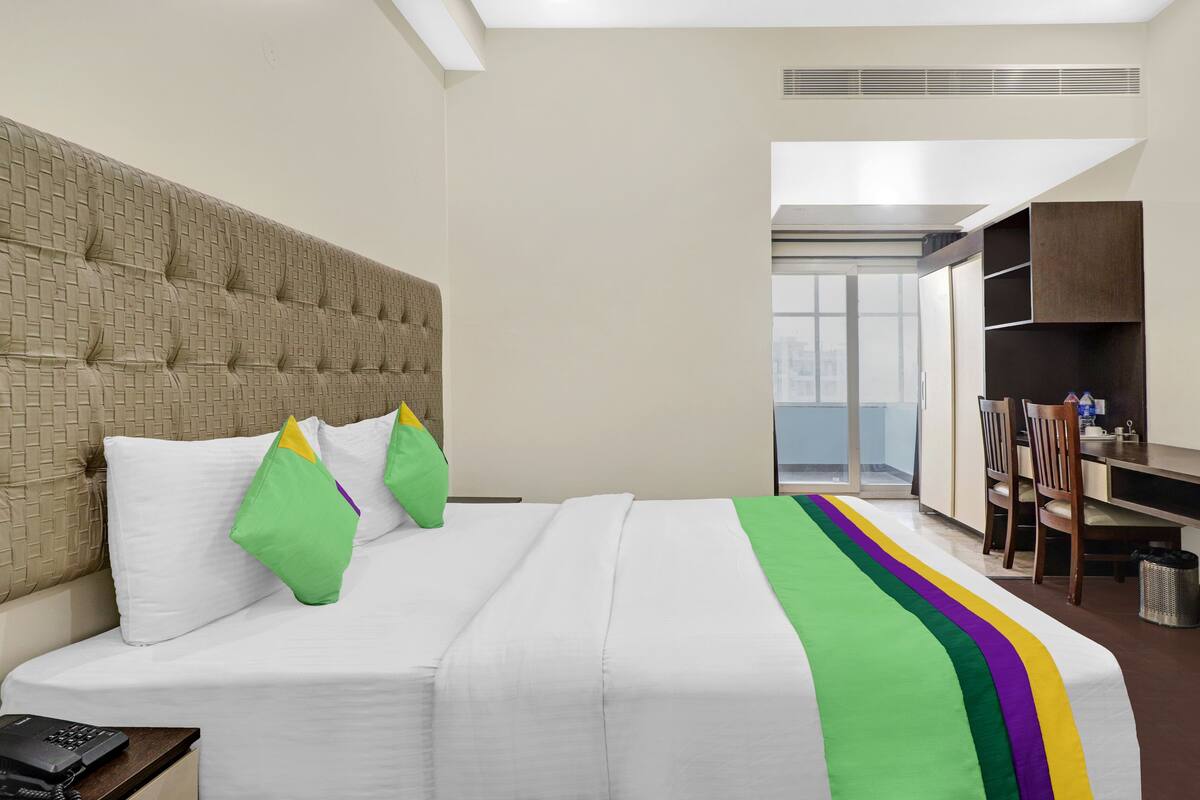 A hotel room with a large bed, a headboard, a desk with a chair, and a view of the outside.