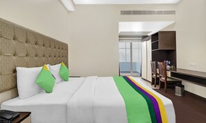 A hotel room with a large bed, a headboard, a desk with a chair, and a view of the outside. - Hotel the Archer (Gurugram)