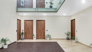 A spacious indoor area with three wooden doors, potted plants, and a mix of dark and light flooring. - Hotel the Archer (Gurugram)