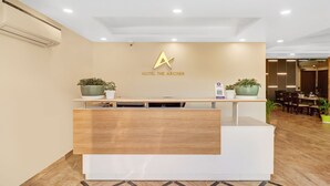 A reception desk with a modern design, featuring a logo above the desk and a sign indicating a phone service. - Hotel the Archer (Gurugram)