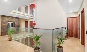 A modern hotel lobby with a glass railing, potted plants, and wooden doors. - Hotel the Archer (Gurugram)