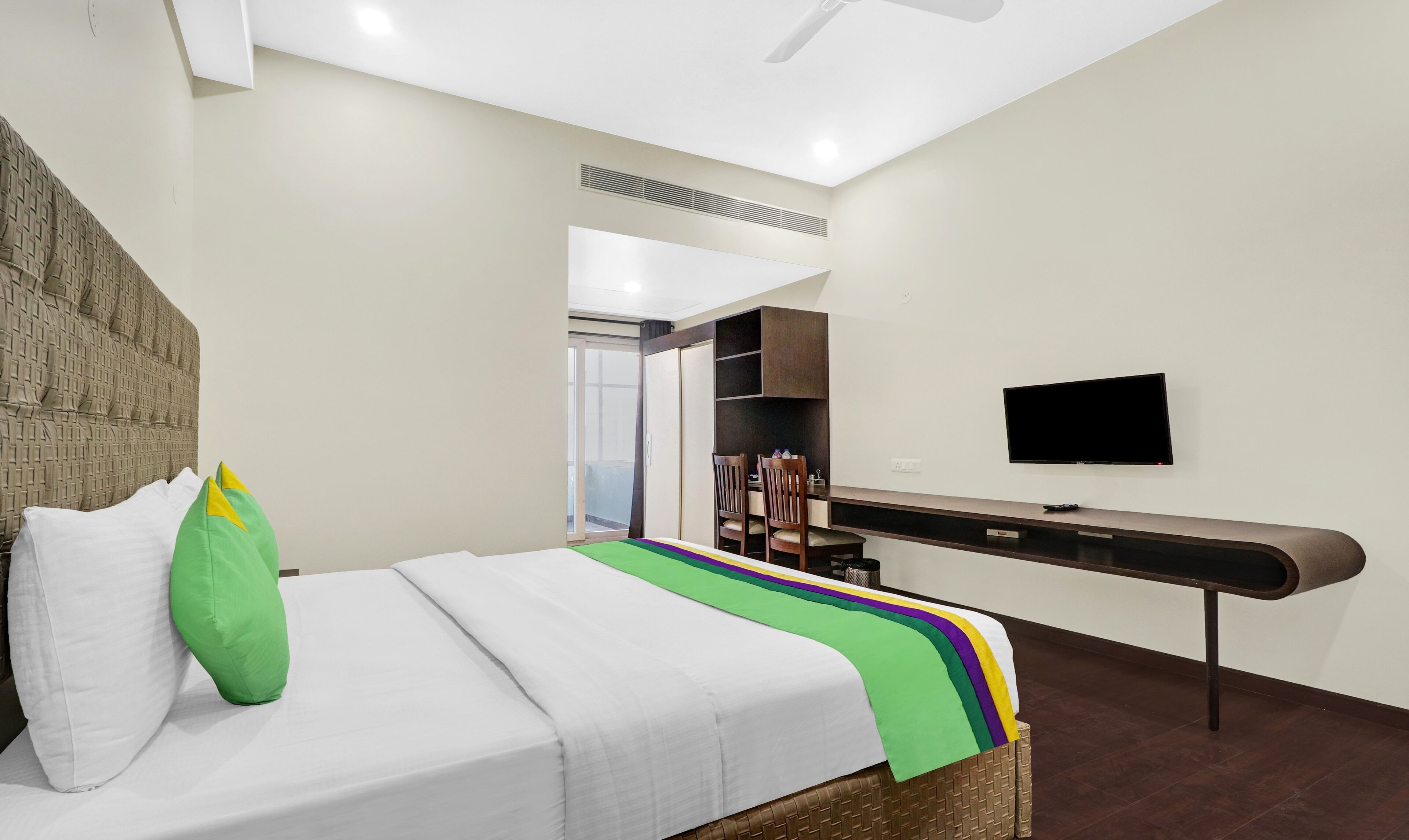 A hotel room with a bed, a TV mounted on the wall, and a wardrobe.