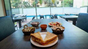A dining table with a sandwich and bowls of food, overlooking a pool and greenery. - Hotel the Archer (Gurugram)
