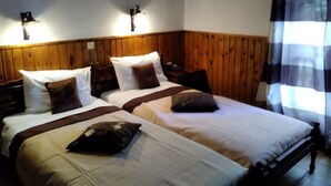 Una cama doble con cabecera de madera, dos mesitas de noche y una ventana con cortina a cuadros.