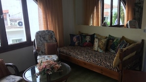 A room with a sofa, a round table with a floral centerpiece, and a chair. - Pettite Morfo (Skiathos)