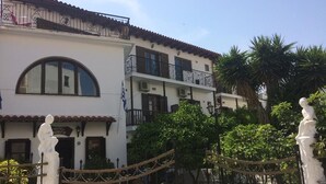 A hotel with a white facade, multiple balconies, and a courtyard with chairs and plants. - Pettite Morfo (Skiathos)