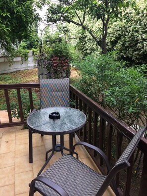 A round glass table with a chair, a small potted plant, and a metal railing on a balcony. - Pettite Morfo (Skiathos)
