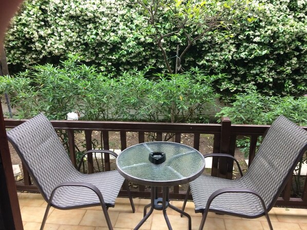 Un patio con dos sillas y una mesa, rodeado por una barandilla de madera y abundante vegetación.