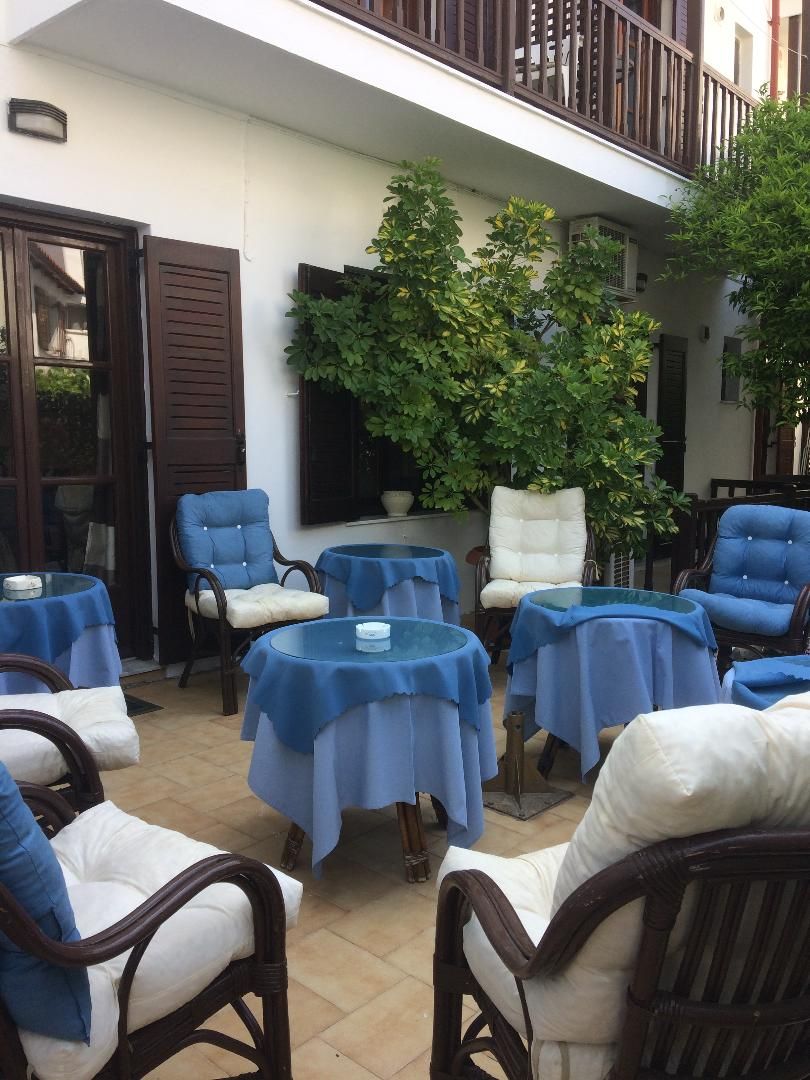 An outdoor seating area with round tables and chairs, a balcony, and a large tree.