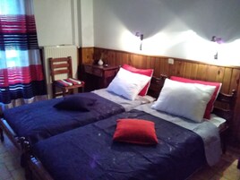 Una cama doble con dos almohadas, una mesita de noche, una silla y una ventana con cortinas.