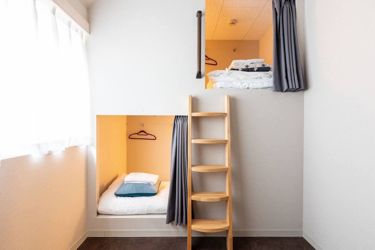 Quarto compacto com beliche, escada de madeira, prateleira pequena e cabideiro.