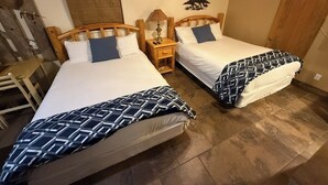 Una habitación con dos camas, cabeceros de madera, una mesita de noche con lámpara y una decoración rústica que incluye una puerta de madera y un adorno de caballo en la pared.