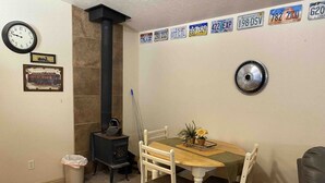 Un comedor con una mesa de madera, sillas blancas, una estufa negra y un reloj en la pared.