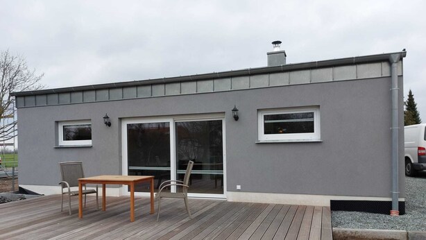 Um edifício moderno com fachada cinzenta, um deck de madeira e uma porta de vidro que dá para um espaço interno.