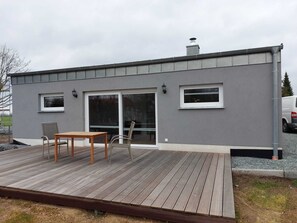 A modern building with a grey exterior, a wooden deck, and a glass door leading to an interior space. - Cozy vacation home (Brünzow)