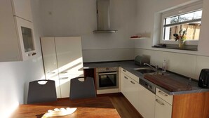 Uma cozinha compacta com área de jantar, incluindo uma mesa e cadeiras de madeira, forno embutido e janela com vista para o exterior.