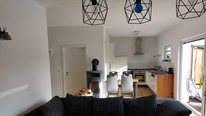 Uma sala de estar moderna com um sofá cinza escuro, uma mesa de centro de madeira e uma cozinha ao fundo.
