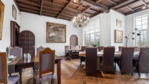 Ein Essbereich mit Holztischen und -stühlen, einer Chandelüster und großen Fenstern.