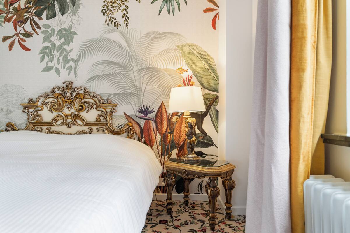 Una habitación de hotel con cama, una mesita de noche con lámpara y un mural en la pared.