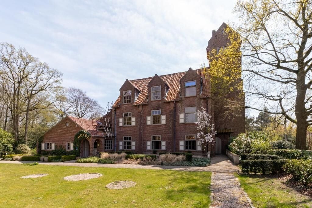 A traditional brick building with a central entrance, multiple windows, and a well-maintained garden with circular flower beds.