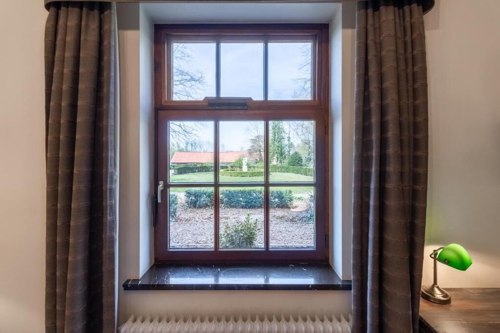 A room with a window, brown curtains, a radiator, and a green desk lamp.