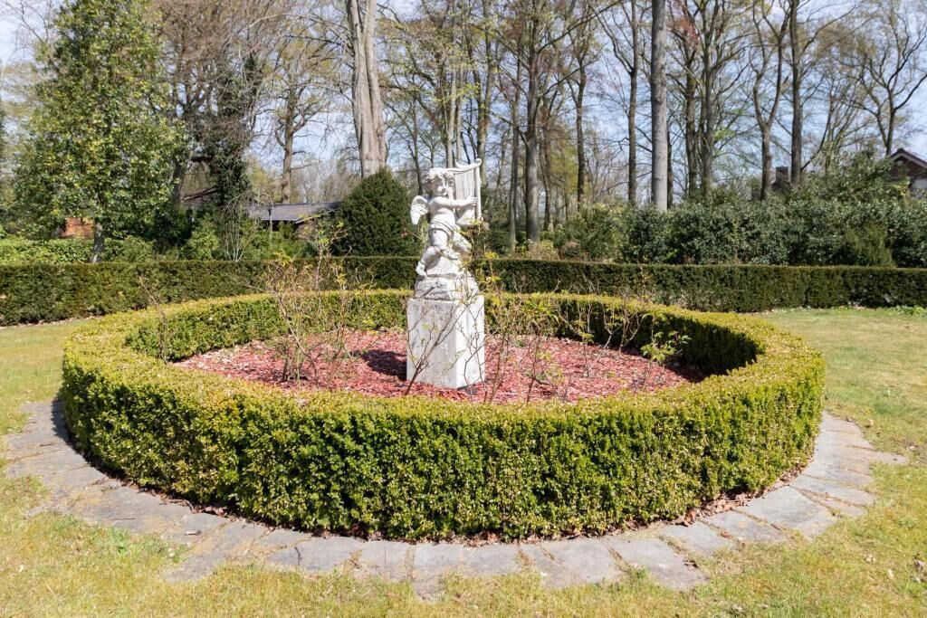 Um jardim circular com uma estátua central rodeada por sebes bem aparadas.