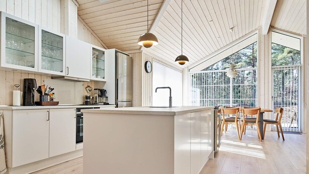 A modern kitchen with white cabinetry, a central island, and a dining area with wooden chairs. - 8 Person Holiday Home in Nexo (Nexø)